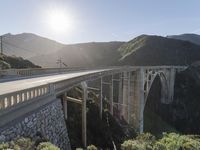 a person on a skateboard on a bridge near mountains with a view of the sun