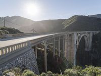 a person on a skateboard on a bridge near mountains with a view of the sun