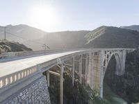 a person on a skateboard on a bridge near mountains with a view of the sun