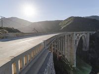 a person on a skateboard on a bridge near mountains with a view of the sun