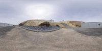 a skateboarder does a trick on a hill covered in gravel and rocks near some big boulders