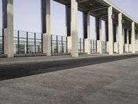 a person rides his skateboard past an empty building on an empty sidewalk with a guard rail