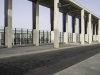 a person rides his skateboard past an empty building on an empty sidewalk with a guard rail