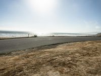 a person riding a skate board on a empty road near the ocean at sunset with sun