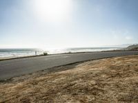 a person riding a skate board on a empty road near the ocean at sunset with sun