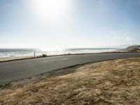 a person riding a skate board on a empty road near the ocean at sunset with sun