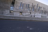 the young man skateboarding on a paved surface by concrete building with windows and doors