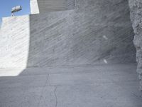 a young man skateboarding near a large concrete wall and stairs in front of a blue sky