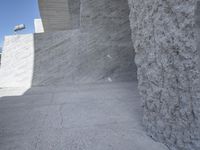 a young man skateboarding near a large concrete wall and stairs in front of a blue sky