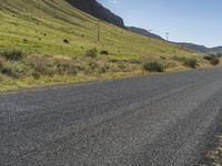 a person riding a skateboard down the middle of a dirt road near grass and mountains