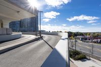 the person on the skateboard rides down the ramp near tall buildings while the sun shines brightly behind