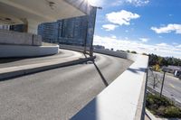 the person on the skateboard rides down the ramp near tall buildings while the sun shines brightly behind