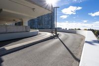 the person on the skateboard rides down the ramp near tall buildings while the sun shines brightly behind