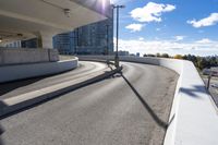 the person on the skateboard rides down the ramp near tall buildings while the sun shines brightly behind