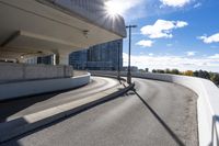 the person on the skateboard rides down the ramp near tall buildings while the sun shines brightly behind