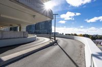 the person on the skateboard rides down the ramp near tall buildings while the sun shines brightly behind