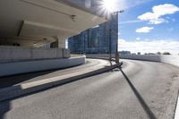 the person on the skateboard rides down the ramp near tall buildings while the sun shines brightly behind