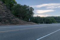 a person riding a skateboard down the highway in front of a hill with trees and sky