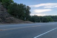 a person riding a skateboard down the highway in front of a hill with trees and sky