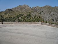 a person riding a skate board next to a hill of rocks with trees in the background