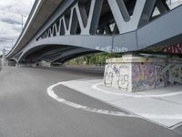 the skateboarder is skateboarding under a bridge with graffiti written underneath it,