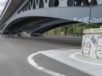 the skateboarder is skateboarding under a bridge with graffiti written underneath it,