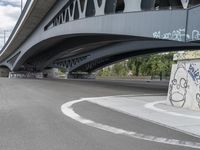 the skateboarder is skateboarding under a bridge with graffiti written underneath it,