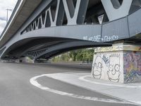 the skateboarder is skateboarding under a bridge with graffiti written underneath it,