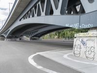 the skateboarder is skateboarding under a bridge with graffiti written underneath it,