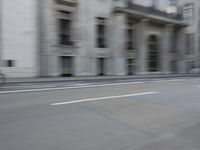 a man on a skateboard is speeding down the road in motion of a blurred building