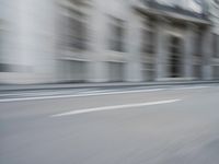 a man on a skateboard is speeding down the road in motion of a blurred building