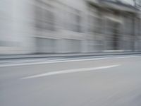 a man on a skateboard is speeding down the road in motion of a blurred building