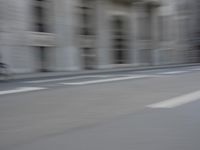 a man on a skateboard is speeding down the road in motion of a blurred building