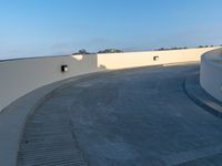 a skateboarder doing a trick on a cement ramp next to white wall with a blue sky