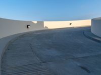 a skateboarder doing a trick on a cement ramp next to white wall with a blue sky