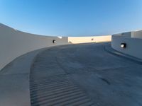 a skateboarder doing a trick on a cement ramp next to white wall with a blue sky