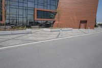 a person riding a skateboard along the side of a road near a building with large windows