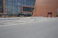 a person riding a skateboard along the side of a road near a building with large windows