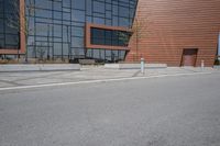 a person riding a skateboard along the side of a road near a building with large windows