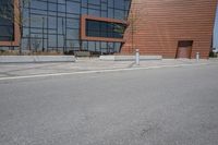 a person riding a skateboard along the side of a road near a building with large windows