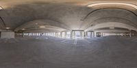 a skateboarder takes a curve on the inside of an empty parking garage filled with concrete, and lights