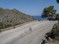 a person rides a skateboard down a rocky street next to the ocean and a mountain side