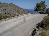 a person rides a skateboard down a rocky street next to the ocean and a mountain side