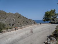 a person rides a skateboard down a rocky street next to the ocean and a mountain side