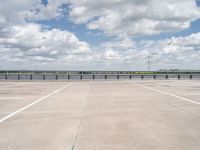 a lone man riding his skateboard across the tarmac of an airport near the water