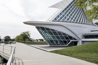 people riding on a skateboard past a building with a curved roof that has large windows