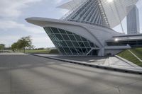 people riding on a skateboard past a building with a curved roof that has large windows