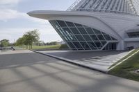 people riding on a skateboard past a building with a curved roof that has large windows