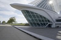 people riding on a skateboard past a building with a curved roof that has large windows