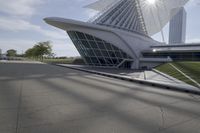 people riding on a skateboard past a building with a curved roof that has large windows